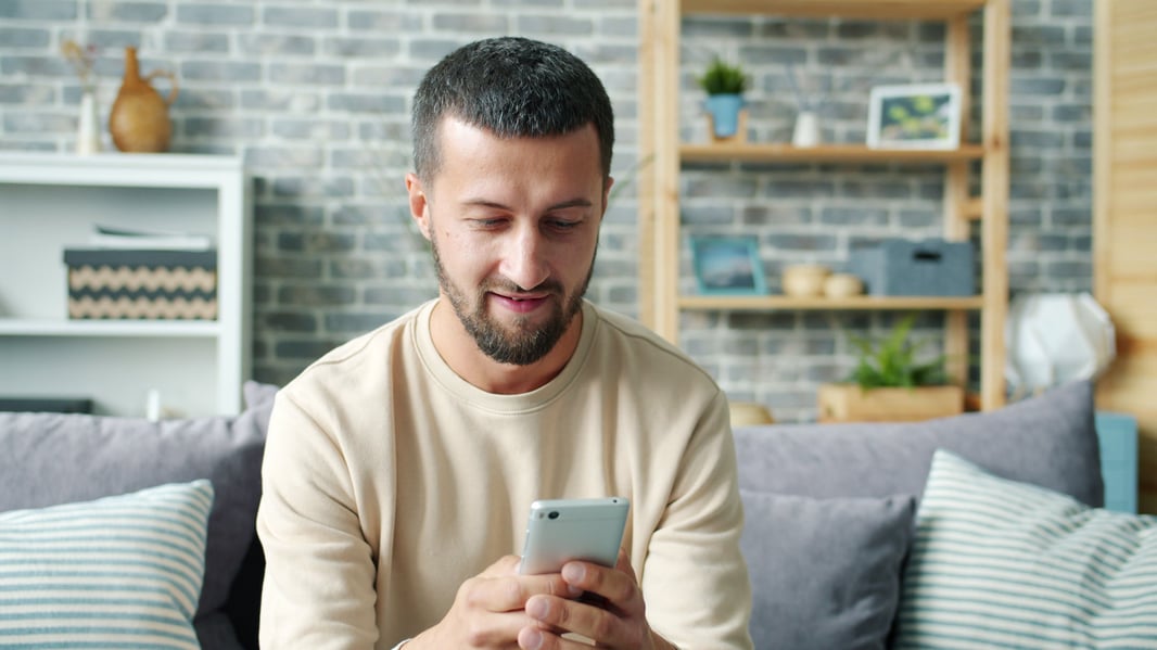 A patient sitting at home on a sofa, completing a form on their phone