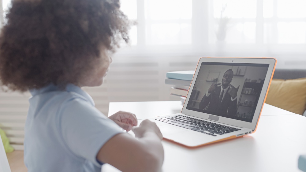 Child sitting at desk with laptop during an online speech therapy session